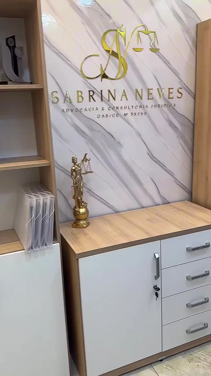 Marca original de Sabrina Neves na parede clara do escritório, com estante e mobiliário de madeira.