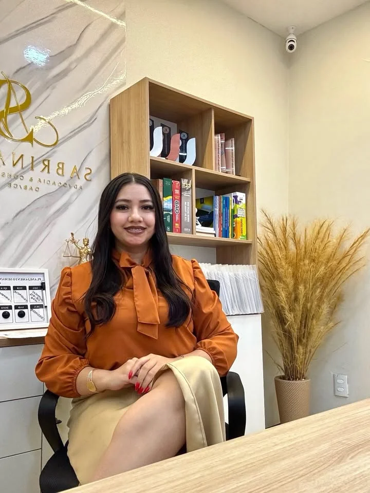 Sabrina Neves em seu escritório, sentada à mesa e sorrindo.